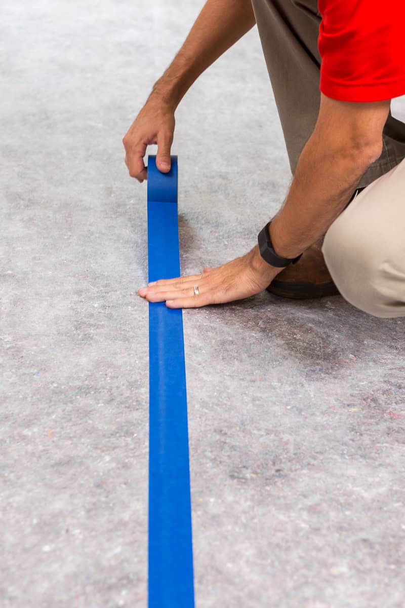 Worker applying blue tape on floor for surface protection at a job site.