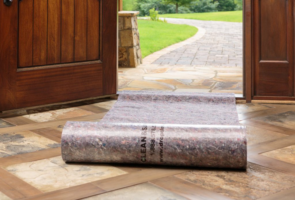 Protective mat rolled out at wooden front door entry, leading to a stone pathway and green lawn.