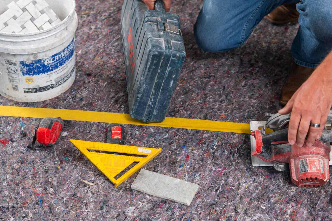 Person preparing tools on protective surface for pro grade work, including a saw, tape, and square.