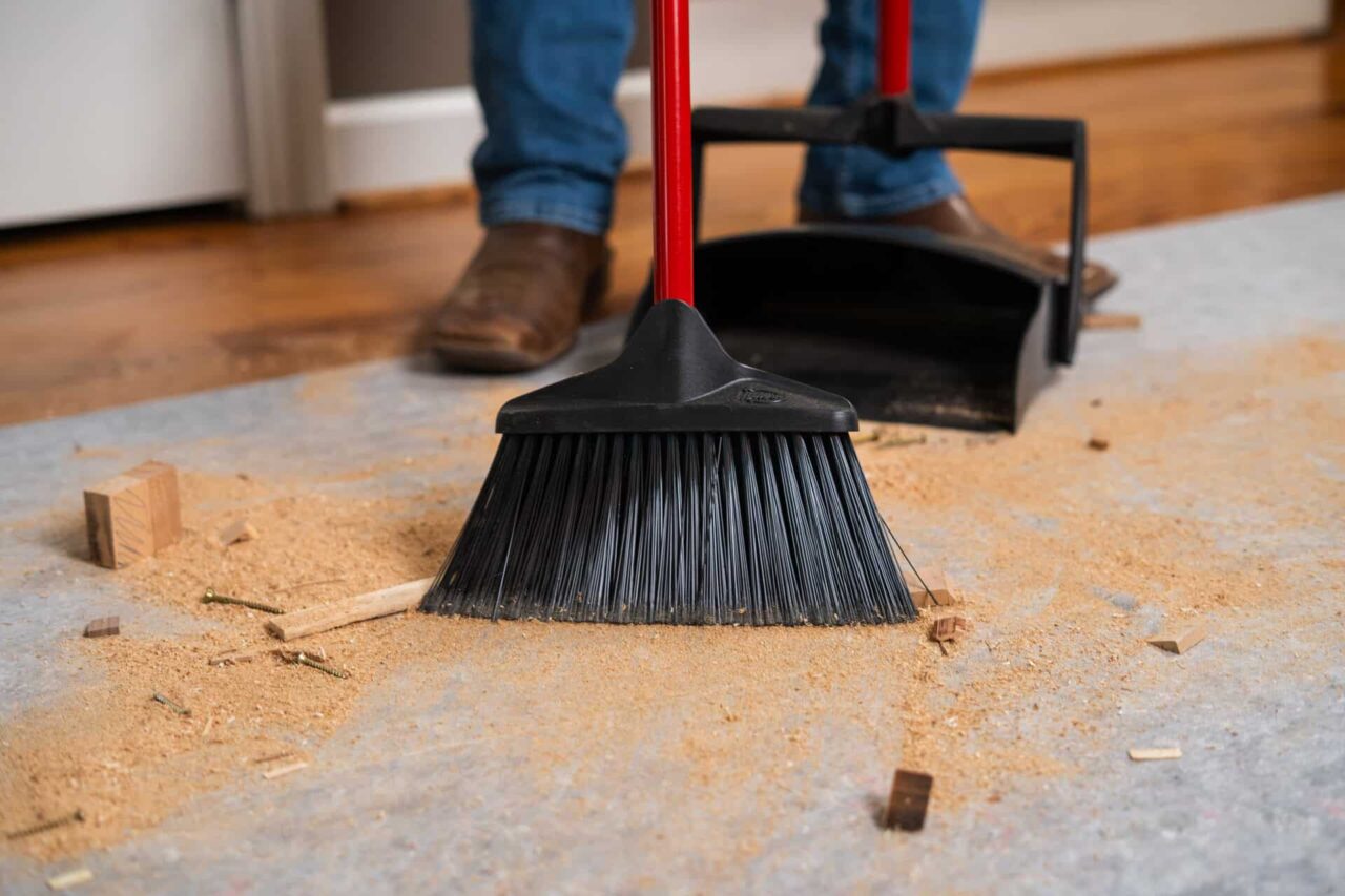 Broom sweeping wood shavings on a Clean&Safe®Pro mat, ideal for leak-proof, skid-resistant protection.