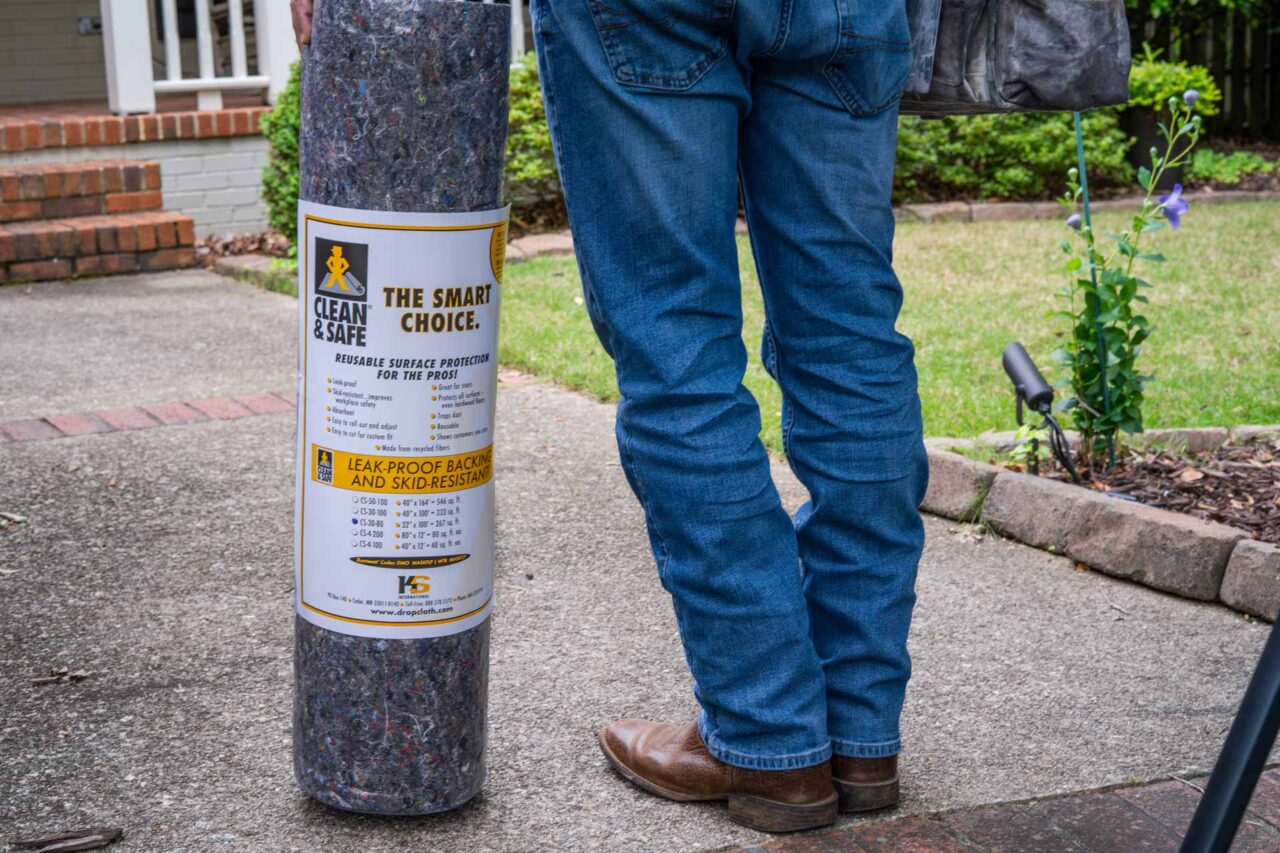 Reusable floor protection roll labeled "Clean & Safe: The Smart Choice" beside person in jeans, outdoors.