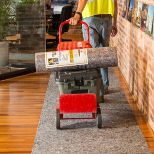 Worker transporting Clean&Safe drop cloth roll and equipment on a cart, ensuring surface protection on hardwood floors.