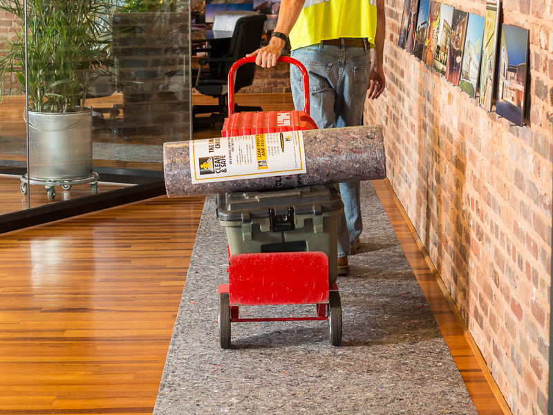 Worker transporting Clean&Safe drop cloth roll and equipment on a cart, ensuring surface protection on hardwood floors.